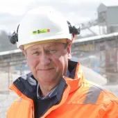 A head and shoulders picture of Mike Phillips, CEO of the British Aggregates Association, wearing orange PPE and a white hard hat, in a quarry.