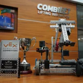 The Vex Robotics Awards on a table in front of a Combilift sign and video display showing a yellow and blue robotic vehicle