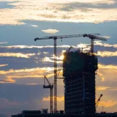 A High rise building under construction in silhouette with the sun setting behind it with three tower cranes