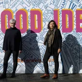 Ruth Sparkes and Sunita Gordon, co-founders of SaferSpace, dressed in black, photographed in harsh sunlight against a map of London with the slogan "Good Idea" printed over it.