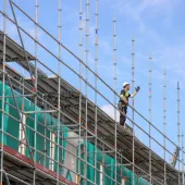 A construction worker in hard hat and PPE working on a scaffold.