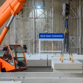 An orange crane and orange PPE-clad worker installing the first platforms at HS2's Old Oak Common station for HS2 trains.