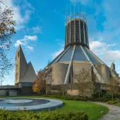 A view of Liverpool Metropolitan Cathedral in early summer with trees and a pond