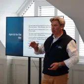 Mike Phillips, CEO British Aggregates Association, wearing a black, fleece gillet, open-necked white shirt and brown chinos, stands in front of a screen, speaking at the BAAs recent Landfill Tax consultation conference.