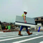 A man in PPE walks across new floor made from Milbank Concrete Products' GDeck, while carrying a panel of the lightweight flooring system.