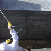 A man in white PPE Waterproofing underground sections of concrete with Vetrofluid using a low pressure pump.