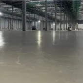 A large, newly poured concrete floor inside a large warehouse