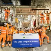 A large group of people in orange PPE, part of HS2 tunnelling team celebrates, TBM Emily completing 5.5km journey. Image: HS2.