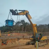 A yellow excavator lifts a blue pile cropper at the Port of Nigg, Scotland