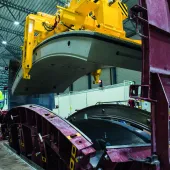A yellow and blue PPE clad worker in a factory uses a mould and lifting device for precast tunnel segments, France, CBE