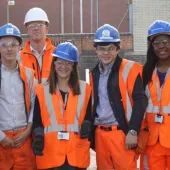 A group of students wearing orange PPE and blue hard hats stand outside a college of FE to celebrate the launch of the The new Construction Technical Excellence Colleges, which will train young people and career switchers in core trades including groundworks and bricklaying.