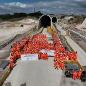 A large crowd of constructions workers in orange PPE stand by the entrance to the recently completed Chiltern Tunnel, HS2’s longest, which is now structurally complete following five years of construction. 