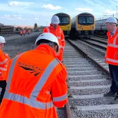 A group of people in Network Rail branded PPE inspect a concrete railway sleeper. The first-generation low-carbon concrete sleepers were installed by Concretene at GCRE in South Wales using 3.75 kg less cement per unit.