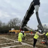 construction workers in yellow PPE lay concrete that's being delivered via chute from a concrete mixer