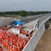 A large group of orange-clad PPE wearing construction workers gather at one end of the colne Valley Viaduct. Over 3,600 m³ of concrete was poured to form the kerb along the 3.4 km Colne Valley Viaduct – now structurally complete.