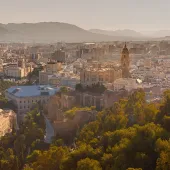 A panoramic photo of Malaga city centre with mountains in the distance, with the bullring lower right and a large church middle left.
