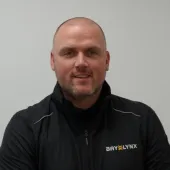 A bald man in a black fleece branded with the Bay-Lynx logo.