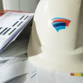 A white hard hat with red and blue insignia, and technical construction papers on a table