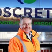 Oscrete director Scott Wilson stand in front of an Oscrete sign wearing orange PPE