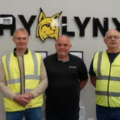 Three men stand in front of the BayLynx logo wearing PPE
