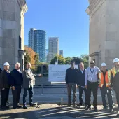 A group of people in business wear and PPE celebrate the use of Bio Graphene Solutions’ graphene-enhanced low-carbon concrete beneath Toronto’s historic Princes’ Gates at Exhibition Place.
