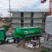 A green, Heidelberg Materials' cement truck in front of an under construction house