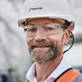 A head and shoulders photo of a man with a beard and glasses wearing PPE and a white hard hat