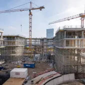 An under construction mid-rise building with two tower cranes in the background