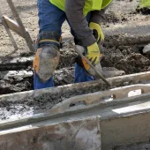 A construction worker using a trowel to help lay concrete foundations