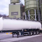 A white, material tanker standing in front of Material Evolution’s Mevo A1 Production Facility in Llay, Wrexham – the UK’s largest producer of ultra-low carbon cement, with a capacity of 120,000 tonnes per year.