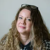 A head shot of Laila Morris, newly appointed practice director at Betts Associates, with long curly hair, a checked top and glasses on her head