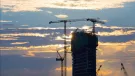 A High rise building under construction in silhouette with the sun setting behind it with three tower cranes