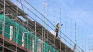 A construction worker in hard hat and PPE working on a scaffold.