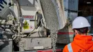 A man in orange PPE and a white hard hat watches low-carbon concrete being delivered for Holcim UK