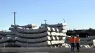 Two men in orange PPE stand next to a stack of precast concrete tunnel segments at the Western Harbour Tunnel Precasting facility in Emu Plains.
