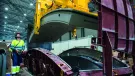 A yellow and blue PPE clad worker in a factory uses a mould and lifting device for precast tunnel segments, France, CBE