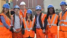 A group of students wearing orange PPE and blue hard hats stand outside a college of FE to celebrate the launch of the The new Construction Technical Excellence Colleges, which will train young people and career switchers in core trades including groundworks and bricklaying.