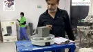 A man with a beard, waring a dark shirt inspects a concrete cube in a testing laboratory.