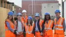 A group of students wearing orange PPE and blue hard hats stand outside a college of FE to celebrate the launch of the The new Construction Technical Excellence Colleges, which will train young people and career switchers in core trades including groundworks and bricklaying.