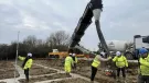 construction workers in yellow PPE lay concrete that's being delivered via chute from a concrete mixer