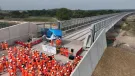 A large group of orange-clad PPE wearing construction workers gather at one end of the colne Valley Viaduct. Over 3,600 m³ of concrete was poured to form the kerb along the 3.4 km Colne Valley Viaduct – now structurally complete.