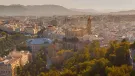 A panoramic photo of Malaga city centre with mountains in the distance, with the bullring lower right and a large church middle left.