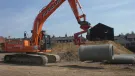 An orange excavator lifts a concrete pipe