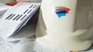 A white hard hat with red and blue insignia, and technical construction papers on a table