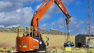 An orange, zero tail-swing midi excavator lifts a pile cropper on a construction site