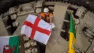 A man wearing a hard hat and waving a Cross of St George flag pokes his head through a TBM cutter wheel with a Welsh flag and another unidentified flag adorning the cutter head as HS2 engineers celebrate the breakthrough of tunnel boring machine Elizabeth at Washwood Heath in Birmingham, completing the 3.5-mile Bromford tunnel under the M6. (Image © HS2 Ltd)