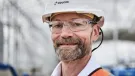 A head and shoulders photo of a man with a beard and glasses wearing PPE and a white hard hat