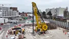 An elevated view of a yellow Soilmec SC-110 Urban cutter working on the Grand Paris Express, constructing 1,200mm-thick diaphragm walls up to 38 metres deep at Rueil–Suresnes Mont-Valérien station, surrounded by houses, low rise buildings and roads.