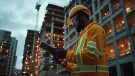 A construction worker in reflective clothing is intently reviewing a digital tablet at a bustling building site.