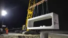 A yellow Kobelco crawler crane lifts a precast, rectangular concrete element